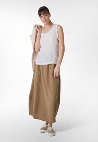 Top de tirantes de lino blanco con dobladillo sin rematar, combinado con una falda marrón de longitud midi y zapatillas beige con cordones blancos. Suéter rosa claro colgado del brazo.