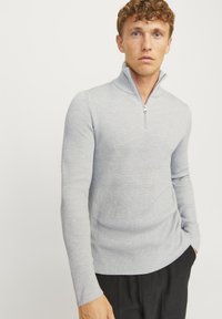 Suéter de rayas de color gris claro con un alto cuello y cierre de media cremallera. Ajustado, de manga larga, con textura suave y sutiles patrones verticales.