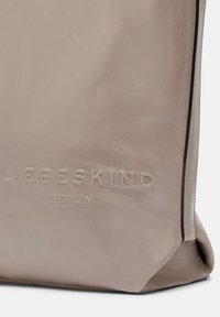 Gros plan sur le coin d'un sac en cuir beige avec le nom de marque « LIEBESKIND BERLIN » en relief et des détails de bord noir.