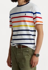 Camiseta de manga corta a rayas en blanco, con rayas horizontales en azul, rojo, naranja, amarillo y marino. Cuello redondo, corte relajado.