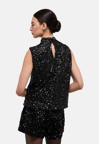 Gilet noir en sequins avec un col montant, un dos ouvert et une coupe ample. Associé à un short assorti en sequins.