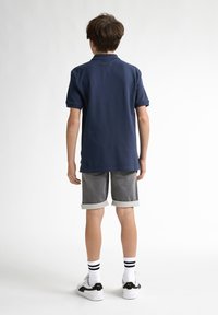 Marinblå pikétröja i bomull, kortärmad, kombinerad med grå uppvikta shorts. Bärs med vita strumpor och svarta sneakers.