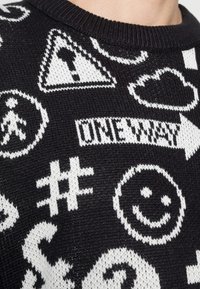 Maglione lavorato a maglia in bianco e nero con vari simboli e icone, tra cui frecce, nuvole e faccine sorridenti; design testurizzato.