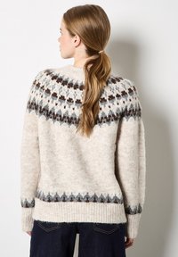 Sweter w kolorze kremowym o miękkiej teksturze, z ozdobnym yaskiem w brązowym i szarym kolorze, prążkowanymi mankietami i dołem oraz luźnym krojem.