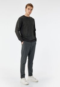 Suéter de manga larga gris oscuro hecho de un tejido texturizado, combinado con pantalones oscuros ajustados y zapatillas blancas. Conjunto casual con líneas limpias.