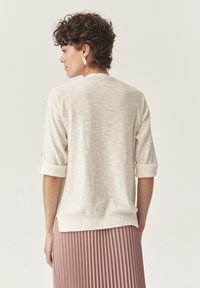 Helle beige Strickoberteil mit halben Ärmeln und umgeschlagenen Bündchen, das einen entspannten Sitz und einen gerippten Saum aufweist, kombiniert mit einem plissierten rosa Rock.