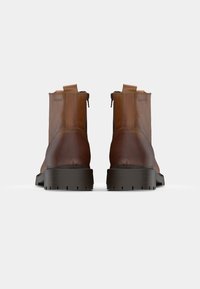 Botas de tobillo de cuero marrón con puntera redonda, paneles laterales elásticos y una suela gruesa de goma negra. Cuentan con tiradores para facilitar su uso.