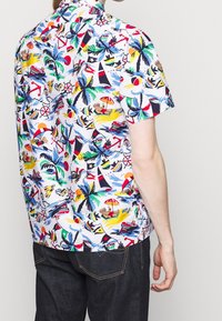 Camisa de manga corta con botones que presenta un fondo blanco con un vibrante estampado tropical, incluyendo palmeras, veleros y escenas de playa.