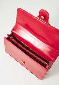 Červená lesklá kabelka so zlatým uzáverom, obsahujúca vnútornú zipsovú priehradku a hladkú textúru. Otvorený dizajn odhaľuje priestranný interiér.