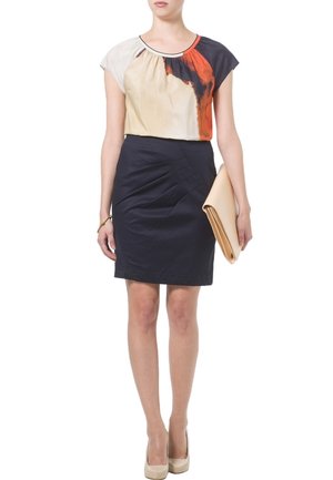 Blusa color block en beige, crema y azul marino con mangas cortas, combinada con una falda lápiz azul marino con detalles plisados y un bolso de mano beige.