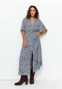 Robe à motif cachemire bleu et blanc avec un décolleté en V, des manches courtes, une taille cintrée et une fente sur le côté, associée à des bottines bourgogne.