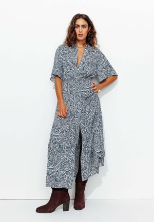 Robe à motif cachemire bleu et blanc avec un décolleté en V, des manches courtes, une taille cintrée et une fente sur le côté, associée à des bottines bourgogne.