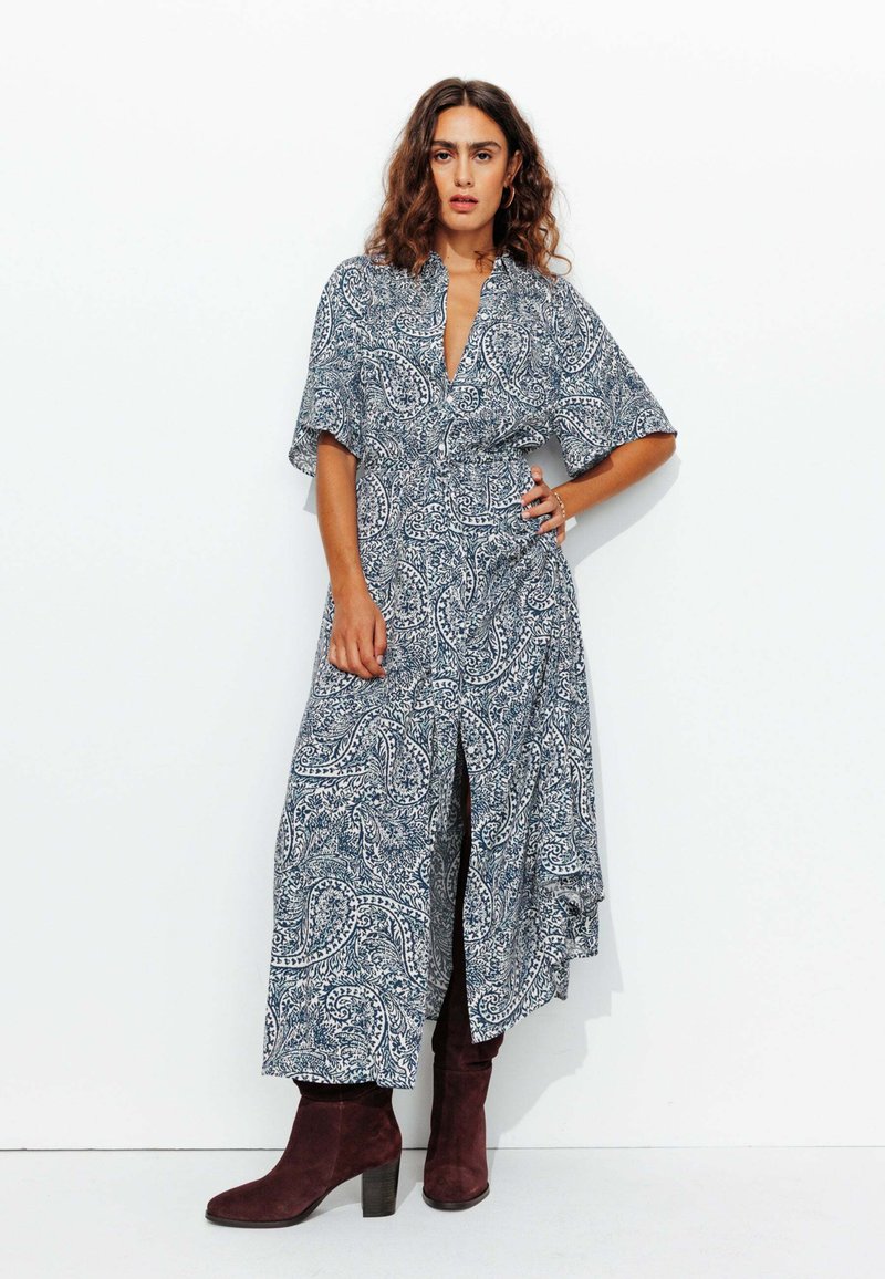 Robe à motif cachemire bleu et blanc avec un décolleté en V, des manches courtes, une taille cintrée et une fente sur le côté, associée à des bottines bourgogne.