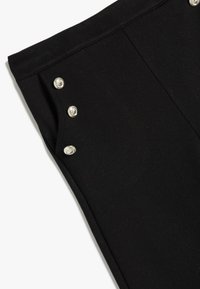 Zwarte broek met een soepele textuur, voorzien van zilveren drukknoopjes aan de zijkant voor accentuering. Tailored ontwerp met strakke lijnen.