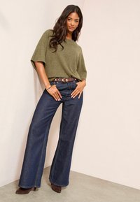 Õlivarvaste roheline oversized-sviiter, millele on sobitatud tumesinised laiad püksid. Pruun nahkline vöö, millel on ümmargune pandla. Pruunid kontsaga säärekingad.