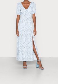 Světle modré květinové maxi šaty s krátkými nafouknutými rukávy, výstřihem do V a bočním rozparkem. Spárovány se světle modrými sandály na blokovém podpatku.