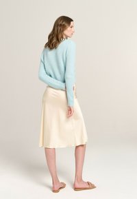 Light blue fuzzy sweater, high-waisted cream satin skirt, and beige sandals. Model shown from the back, with hair slightly wavy.