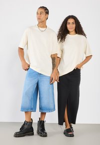 Kremfargede oversized t-skjorter, lyseblå denim vide shorts, svart denim lang skjørt, svarte støvler og slip-on sko med teksturert såle.