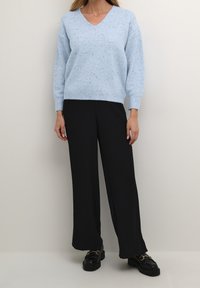 Jasnoniebieski sweter z dzianiny z dekoltem w serek i ściągaczami przy mankietach, zestawiony z czarnymi spodniami o szerokich nogawkach i czarnymi platformowymi butami.