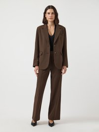 Fato castanho personalizado com um blazer ligeiramente oversized featuring dois botões, combinado com calças de perna reta e sapatos pretos de bico apontado.