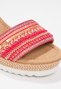 Sandale à talon compensé beige avec semelle en jute tissée et large bride en tissu rouge ornée de sequins dorés et de perles à l'avant.