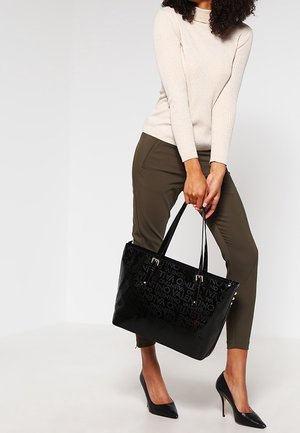 Zwarte glanzende tote bag met reliëflogo-ontwerp, dubbele handvatten, rechthoekige vorm en accenten in goudkleurig beslag.