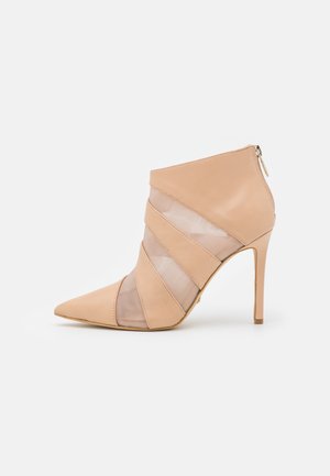 Bottine à talons aiguilles beige avec un embout pointu, dotée de superpositions de tulle nude et de cuir lisse, avec une fermeture éclair à l'arrière.