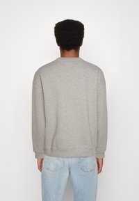 Sudadera gris con cuello redondo y mangas largas, con puños y dobladillo acanalados, combinada con jeans de color azul claro. Tejido suave y texturizado.