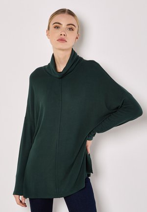 Oversized, mørkegrøn bluse med cowl-hals og lange ærmer, der har en blød tekstur og sideslids for ekstra komfort og bevægelsesfrihed.