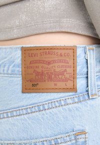 Läderpatch från Levi Strauss & Co. på ljusblå denimjeans, kombinerat med en beige ribbad topp som visar midja och sömnadsdetaljer.