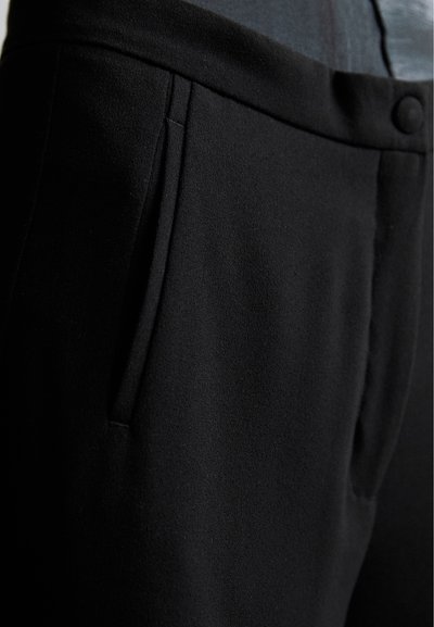 Black tailored pants made of smooth fabric with a slim fit, side pockets, and a concealed button closure. No patterns or visible hardware.