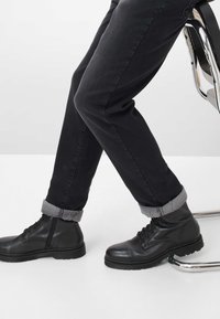 Jeans neri con risvolti che mostrano un motivo a pois bianchi, abbinati a stivali in pelle nera con lacci e suola texturizzata.