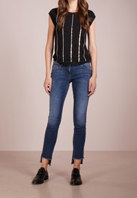 Top negro con rayas metálicas verticales, combinado con jeans ajustados azules con dobladillos deshilachados. El calzado son zapatos negros de tacón bajo.
