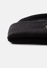 Must üksik musta kootud beanie, millel on ribakujuline tekstuur, volditud serv ja väike logotäpiga silt küljes. Pehme materjal, loodud soojuse tagamiseks.