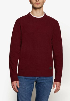 Burgundy strikket sweater med lange ærmer, rund hals og ribbede mansjetter. Har et lille mærke med branding nederst til venstre.