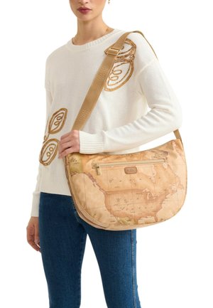 Donna con maglione bianco e jeans blu che tiene una borsa a tracolla color cuoio con stampa di una mappa del mondo vintage e tasca frontale con cerniera.