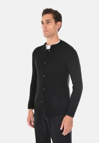 Cardigan nero a coste con scollatura rotonda, bottoni frontali e due tasche inferiori. Realizzato in un tessuto a maglia testurizzata.
