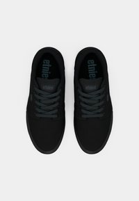 Μαύρα χαμηλά Sneakers με λείο ύφασμα στην επάνω πλευρά, σχέδιο με κορδόνια, και δίχρωμες μαύρες και γκρίζες λεπτομέρειες στην πατούσα και τα κορδόνια.