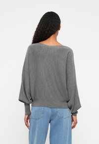 Suéter cinza de malha com uma silhueta relaxada, apresentando um decote largo e mangas balão, combinado com jeans de perna reta azul claro.