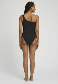 Maillot de bain noir à épaule dénudée avec un motif texturé et des jambes hautes, affichant un design élégant et moulant.