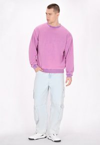 Felpa crew neck color lavanda, con polsini a coste, abbinata a pantaloni cargo azzurri chiari con tasche laterali, completata da sneakers bianche.