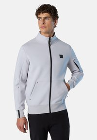 Giacca zip grigia chiara con collo alto, due tasche frontali, dettagli neri e logo. Realizzata in materiale morbido e testurizzato.