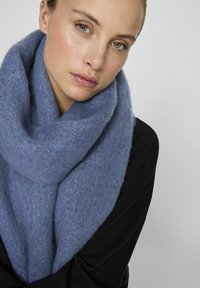 Sciarpa a maglia di un azzurro chiaro, morbida e avvolta loosely attorno al collo. Realizzata in materiale soffice, con una finitura testurizzata e una forma cilindrica.