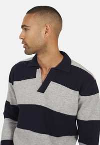 Pull rayé bleu marine et gris avec un col et une fente en V à l'avant. Tissu tricoté texturé, présentant des rayures horizontales de largeurs variées.