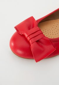 Punaisen nahkaiset ballerinat, joissa on pyöreä kärki ja suuri, jämäkkä nauha aksenttina. Sisäpohjassa on pieniä reikiä ilmanvaihtoa varten.