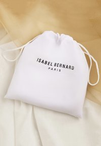 Weißer Zugbeutel aus glattem Stoff mit einem schwarzen Logo, das "ISABEL BERNARD PARIS" zeigt. Einfaches Design mit einer weichen Textur.