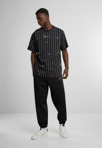 Black striped t-shirt with white anchor patterns, relaxed fit, paired with black tapered sweatpants and white sneakers. Smooth fabric texture.