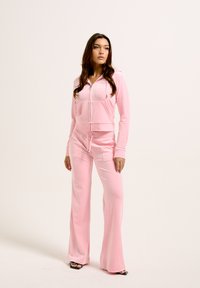 Ensemble de survêtement rose comprenant un hoodie crop zippé avec poches avant et un pantalon évasé assorti, fabriqué en matériau doux et lisse.