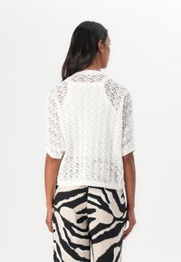 Pull en tricot blanc avec un design texturé et aéré, à manches courtes. Associé à un pantalon rayé noir et blanc façon zèbre.