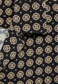 Zwarte stof met een herhalend bloemenpatroon in beige, bruin en wit, met ingewikkelde details en een zachte textuur.